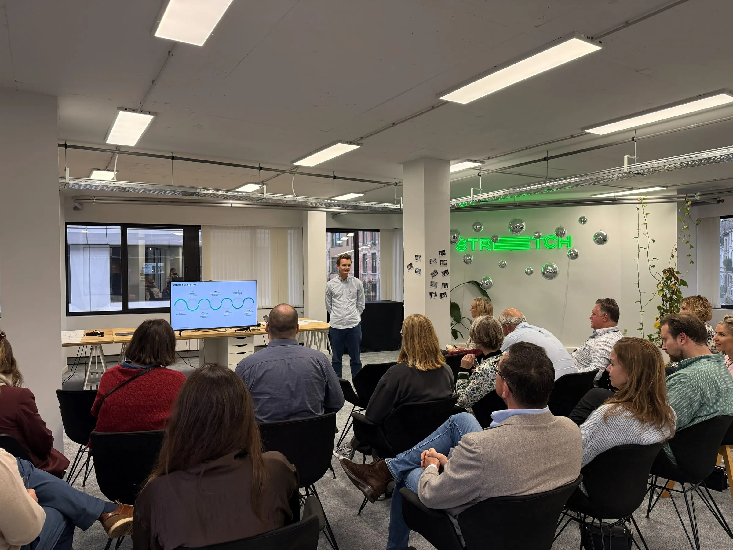 Een volle zaal tijdens een eerdere sessie van Stretch Innovation in Antwerpen, met de spreker vooraan en het Stretch-neonlogo op de achtergrond.